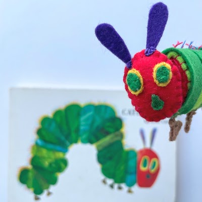 The Very Hungry Caterpillar with the book of the same name in the background.